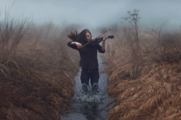 Chica hasta las rodillas en un arroyo tocando el violín