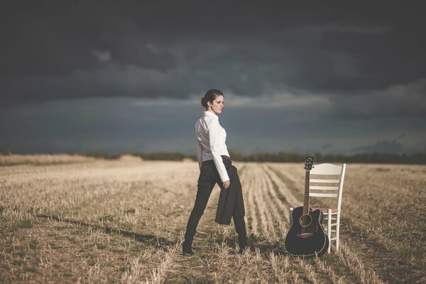 Una chica con una camisa blanca de negocios en el campo con una guitarra y una silla