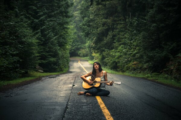 Ragazza con chitarra seduta in mezzo alla strada