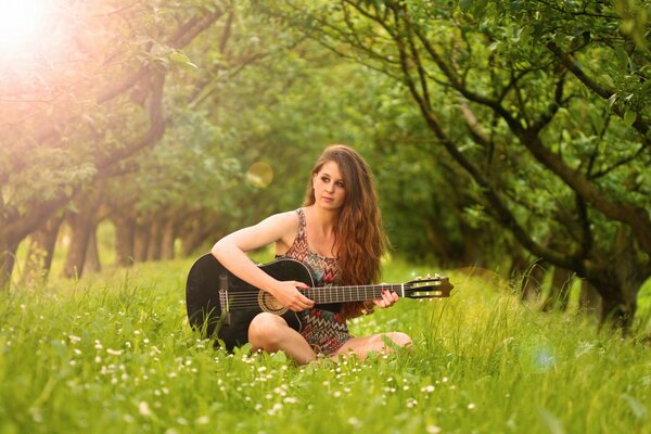 A girl plays guitar in a green clearing