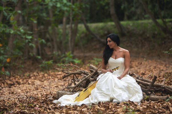 Ein Mädchen im Hochzeitskleid sitzt mit einer Gitarre im Wald