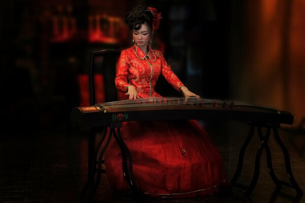 Belleza Oriental en vestido rojo juega en Guqin