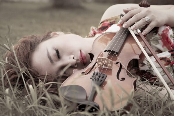 Niña yace con el violín en la hierba