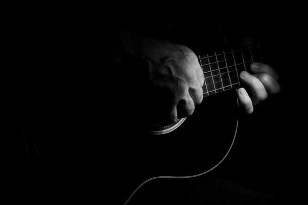Mano en las cuerdas de la guitarra en la oscuridad