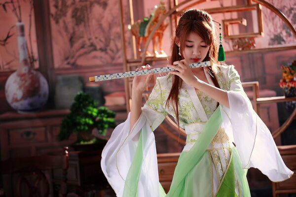 Fille asiatique en robe blanche et verte joue de la flûte