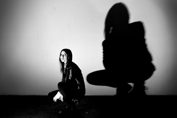 Ein Mädchen hockt auf einem grauen Hintergrund spiegelt ihren schwarzen Schatten wider