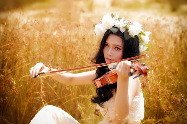 La chica de la corona toca el violín en el campo