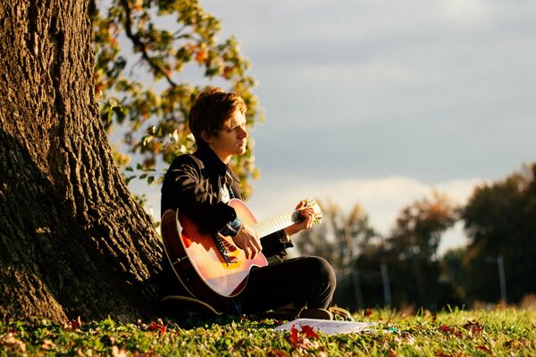 Un chico triste con una guitarra bajo un árbol