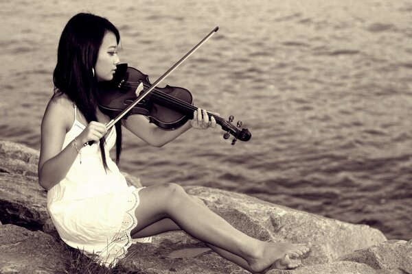 Asian woman playing the violin on the background of the water surface