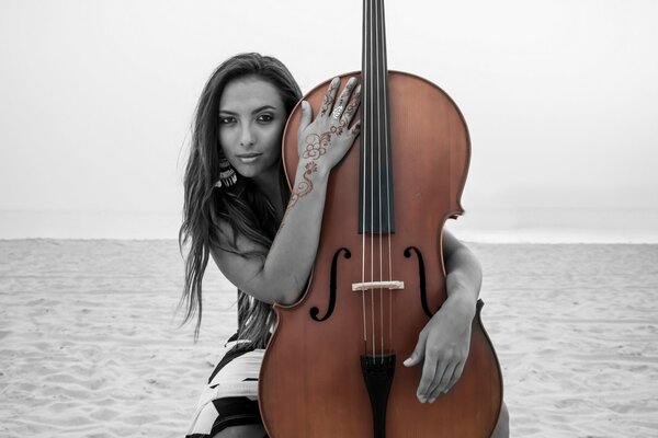 A girl on the sand hugs a double bass