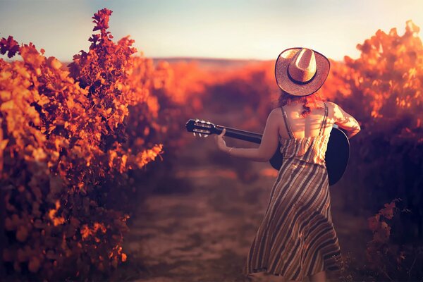 Una chica con un sombrero con una guitarra en el fondo de un viñedo