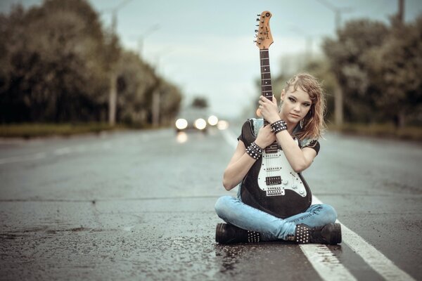 A girl with a guitar in the middle of the road