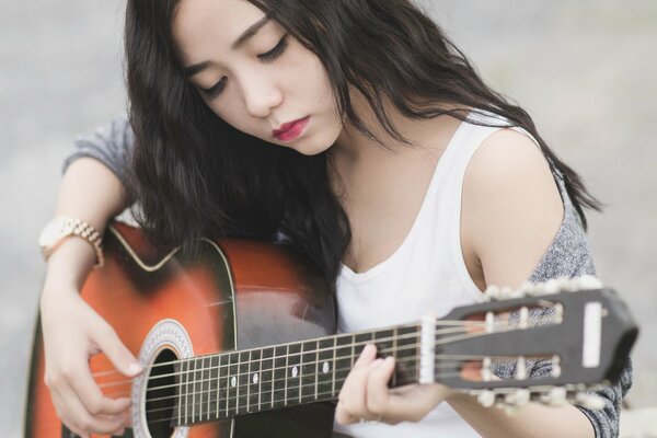 Tocar la guitarra chica asiática con el pelo largo