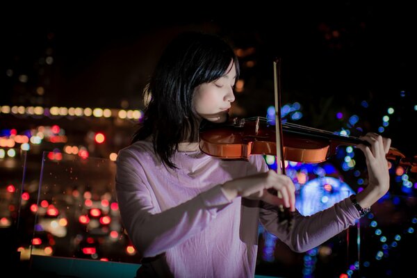 A girl plays the violin against the background of a night city