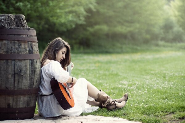 A girl with a guitar is sitting near a barrel