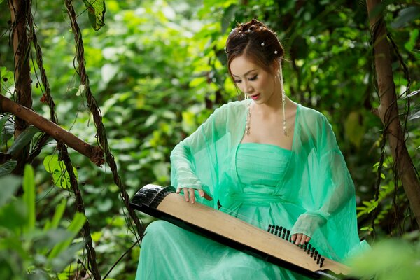 Asiatische Mädchen im grünen Kleid spielt ein Musikinstrument