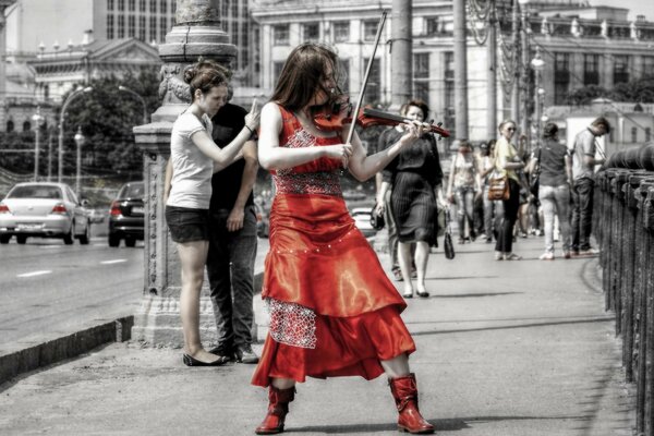 Девушка в красном играет на скрипке посреди улицы