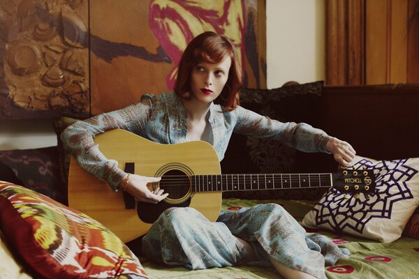 A red-haired girl tunes an acoustic guitar