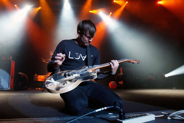 Tom DeLonge na kolanach gra na gitarze