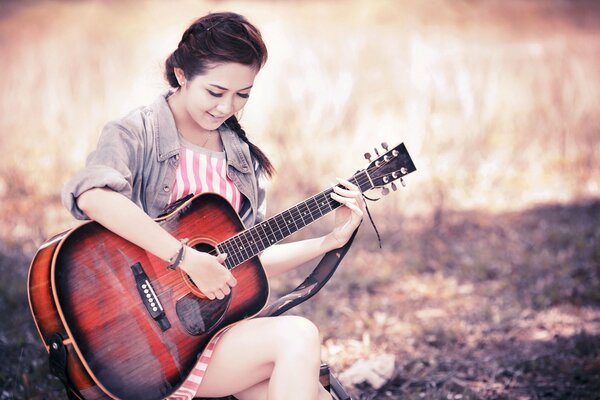 A girl plays the guitar while sitting in nature