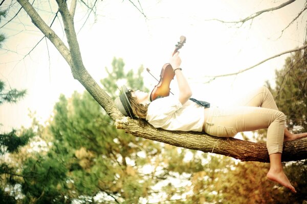 A girl is lying on a tree with a violin in her hands