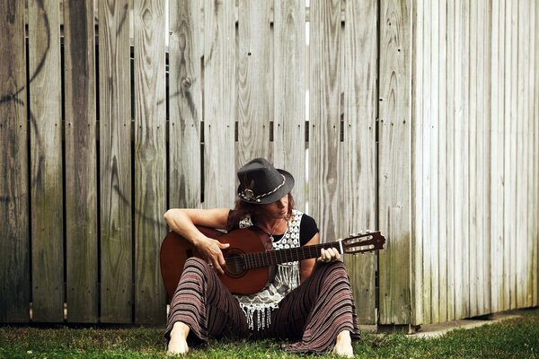 Joven guitarrista con sombrero cerca de la valla