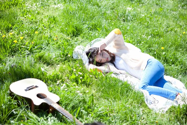 The girl singer is lying with a guitar on the grass