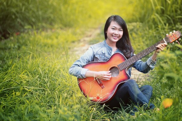 Canzoni sotto la chitarra su una radura verde ragazza asiatica