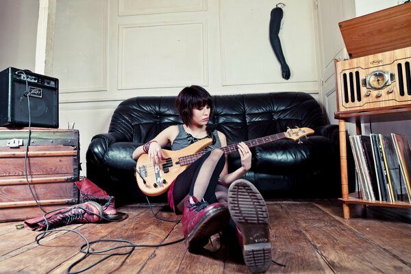 The girl is sitting on the floor and playing the guitar