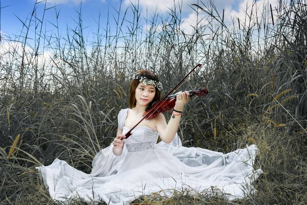 The girl is sitting in the grass and playing the violin