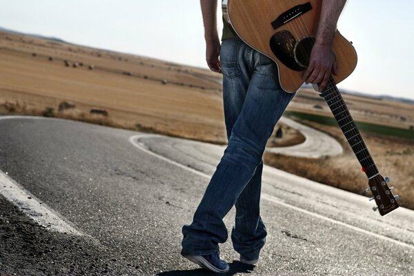 A man with a guitar is walking down the road