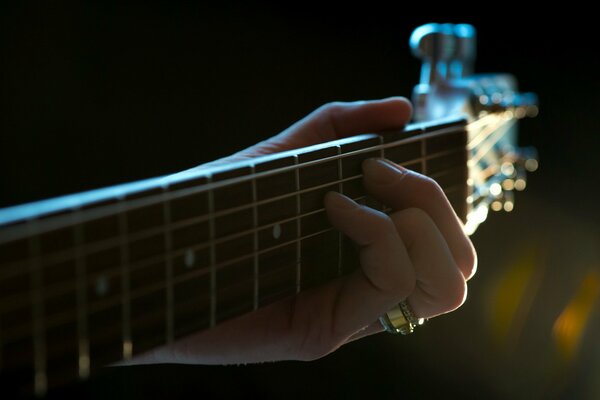 The hand clamps the strings of the guitar