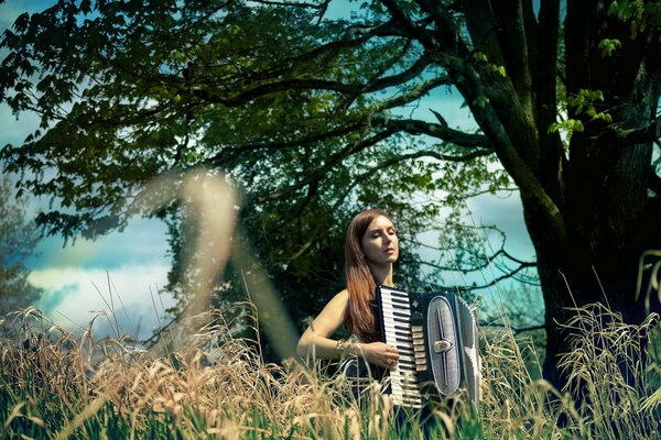 A girl with an accordion on the background of nature