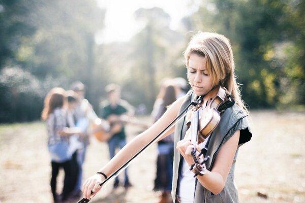 An adult girl plays the violin against the background of people