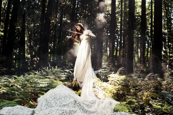 A girl with a violin in a white dress against a forest background