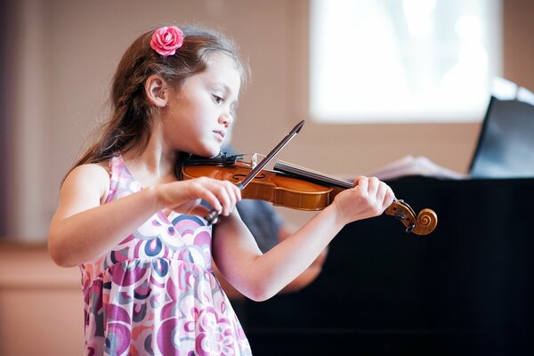 A little girl in a pink floral dress plays the violin