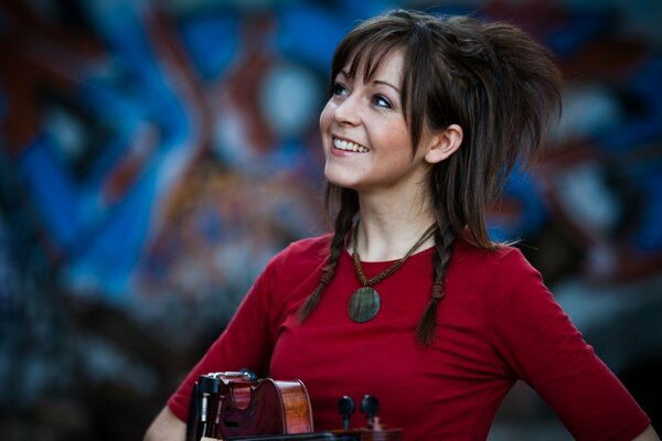 Lindsey Stirling mit einer Geige an der Wand mit Graffiti