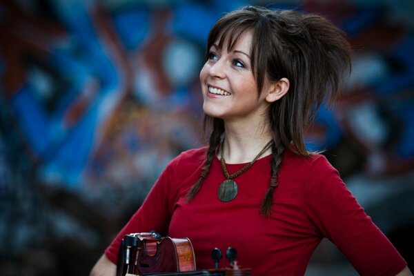 Lindsay Stirling with a violin against a graffiti wall