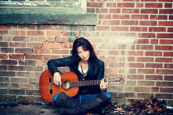 Una chica con una guitarra en una pared de ladrillo