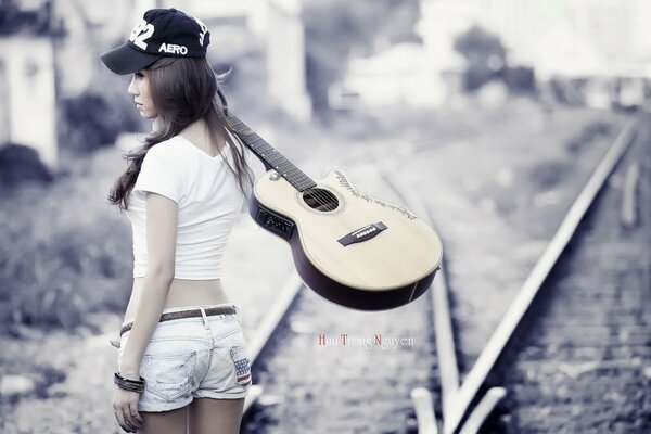 Chica con guitarra en los rieles del tren