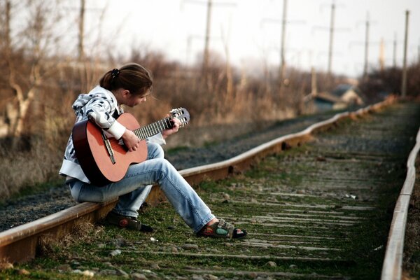 Dziewczyna gra na gitarze, siedząc na szynach