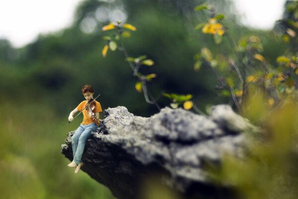 A boy plays the violin against the background of nature