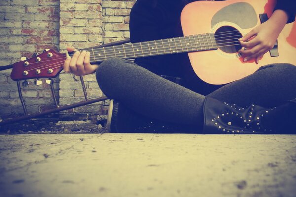 The girl is sitting and playing the guitar