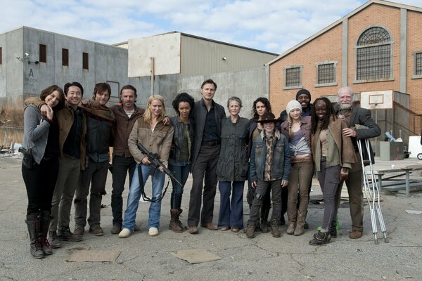 Photo de groupe des acteurs souriants de la série The Walking Dead sur le fond des décorations de maisons