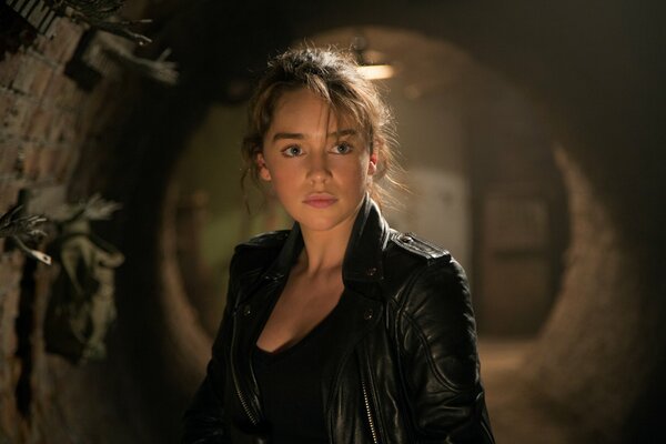 Fotograma de la película Terminator: Génesis, donde la heroína de Emilia Clarke se encuentra en una chaqueta de cuero contra el fondo de una bóveda de piedra