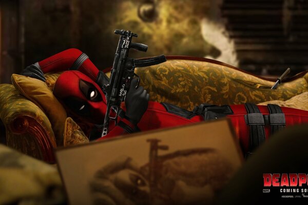 Deadpool is lying with a machine gun on the couch