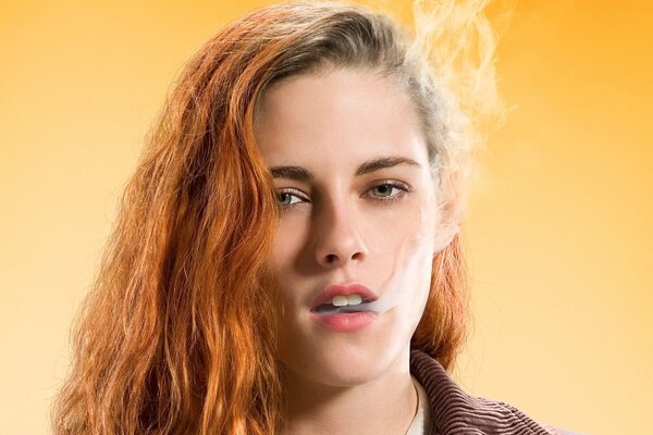 Kristen Stewart con el pelo rojo exhala humo sobre un fondo amarillo