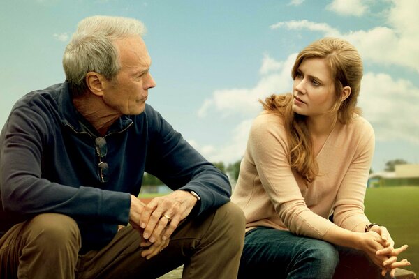 Clint Eastwood and Amy Adams sit on the field