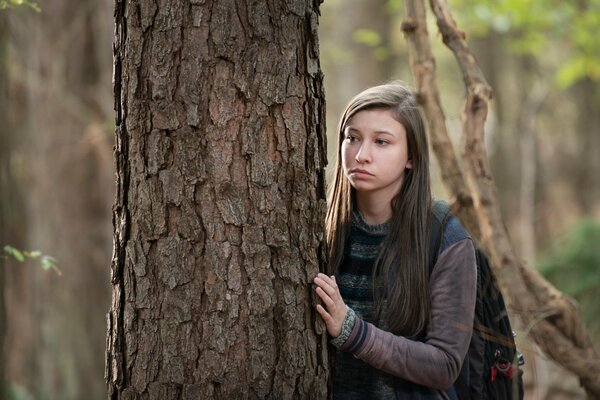 La heroína asustada se esconde detrás de un árbol en el bosque