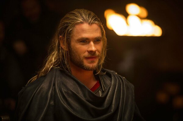 Thor with long hair stands against the background of a torch